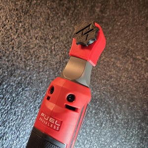 May include: A red and black cordless power tool with a black star-shaped knob on the top. The tool is labeled "FUEL BRUSHLESS".