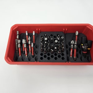 May include: A red plastic tool organizer filled with various drill bits and accessories. The bits are arranged in a black foam insert, with red accents on the tools. The organizer is rectangular and sits on a white surface.