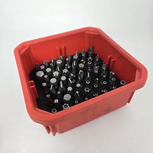 May include: A red plastic container filled with a variety of screwdriver bits. The bits are arranged in a grid pattern and are made of metal.