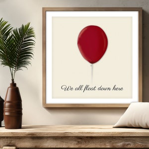 May include: A framed print featuring a red balloon on a cream background with the text "We all float down here" in a black script. The print is in a wooden frame. Decorative vases and a plant are on a wooden surface.