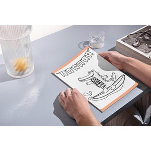 May include: A black and white illustration of an alligator wearing a swimsuit and riding a surfboard. The illustration is on a white card with an orange border. The text "SUMMER" is written in a banner above the alligator.