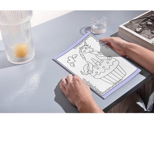May include: A black and white coloring page featuring a unicorn sitting on a cupcake. The unicorn has a horn, mane, and tail. The cupcake has sprinkles and a cherry on top. The page is surrounded by a decorative border.