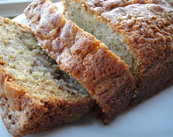 May include: A loaf of freshly baked banana bread, sliced to reveal a moist interior. The bread has a golden-brown crust and a soft, textured crumb. The slices are arranged on a white plate, showcasing the homemade treat.