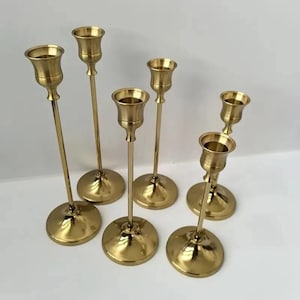 May include: Set of six gold metal candle holders with varying heights. The candle holders have a simple design with a round base and a cup for holding a candle.