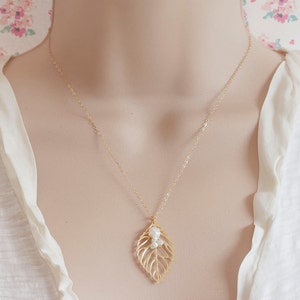May include: A gold chain necklace with a delicate gold leaf pendant accented with small white pearls.