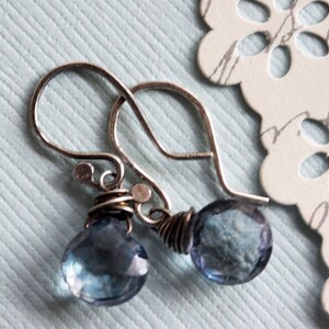 May include: Silver earrings with blue gemstone drops. The earrings have a delicate, handcrafted look.
