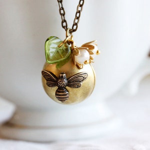 May include: A gold necklace with a bee charm, green glass heart charm, and white pearl flower charm.