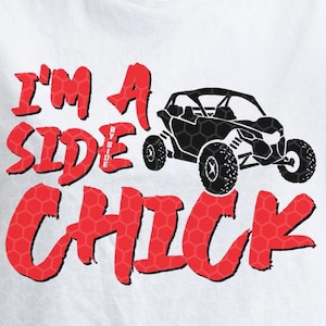 May include: White t-shirt with the text "I'M A SIDE CHICK" in red and a black graphic of an off-road vehicle. The text has a honeycomb pattern. The shirt is a casual wear item.