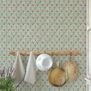 May include: A kitchen scene featuring a light green floral wallpaper with a repeating pattern of pink, blue, and yellow flowers. A wooden rack holds two white towels, a white colander, and two wooden cutting boards. A lavender plant is in the foreground.
