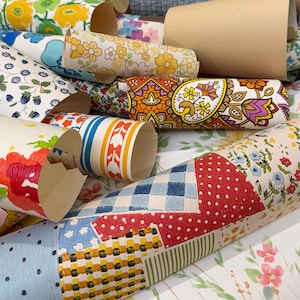 May include: A collection of rolled wallpaper samples featuring various patterns including floral prints, paisley designs, geometric shapes, gingham checks, and polka dots in a vibrant color palette of red, blue, yellow, orange, green, and white.