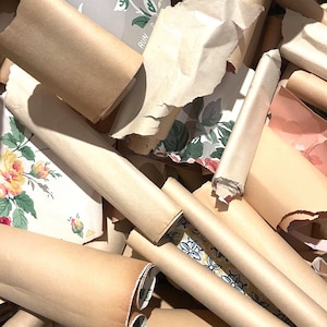 May include: A collection of rolled paper scraps and fragments featuring various patterns, including yellow roses on a white background, blue floral motifs, and solid brown paper. The assortment includes torn edges and layered textures.