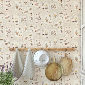 May include: A kitchen scene featuring a cream-colored wallpaper with a repeating pattern of food and drink illustrations. A wooden rack holds two light gray towels, a white colander, and two wooden cutting boards. Lavender plants are in the foreground.