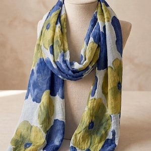 May include: A lightweight scarf with a floral pattern in shades of blue, yellow, and white. The scarf is draped over a mannequin, showcasing its flowing fabric and design. The scarf's pattern features large, abstract flower shapes.