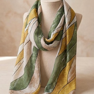 May include: A long rectangular scarf featuring a repeating abstract pattern of flowing, curved bands in shades of olive green, mustard yellow, and off-white. The fabric displays a subtle, mottled texture throughout, with thin black lines outlining each distinct color section.