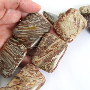 May include: A strand of brown, white, and gold square-shaped gemstone beads. The beads have a marbled pattern.