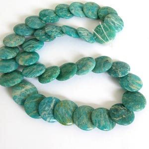 May include: A strand of turquoise green amazonite gemstone beads. The beads are round and flat, with a smooth, polished finish. The beads are strung on a white thread.