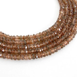 May include: A strand of brown faceted gemstone beads. The beads are small and have a slightly irregular shape. The beads are strung on a clear thread.