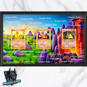 May include: A framed display of three Pokémon trading cards: Charmander, Charmeleon, and Charizard. The cards are set against a backdrop of a volcanic landscape with purple mountains and green grass. The frame has the text "Dragon Slabs" repeated.