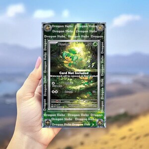 May include: A graded trading card featuring a green and yellow cartoon character, Pansage, in a forest setting. The card is encased in a clear plastic holder with the text "Dragon Slabs" and "Card Not Included".