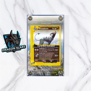 Könnte beinhalten: Eine Houndoom Pokémon-Karte in einem transparenten Schutzgehäuse. Die Karte zeigt eine schwarz-graue Houndoom-Illustration auf gelbem Hintergrund. Das Gehäuse trägt die Aufschrift "Dragon Slabs" und "Custom TCG Cases".