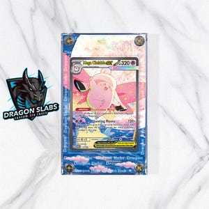 May include: A Pokémon trading card encased in a clear, blue-edged holder. The card features a pink Mega Clefable character with the text "Mega Clefable EX" and "320". The holder has the text "Dragon Slabs" printed on the edges.