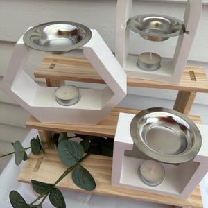 Könnte beinhalten: Drei weiße Keramik-Räucherbrenner mit Metallschalen und Teelichthaltern. Die Brenner sind auf einem mehrstufigen Holzständer angeordnet.