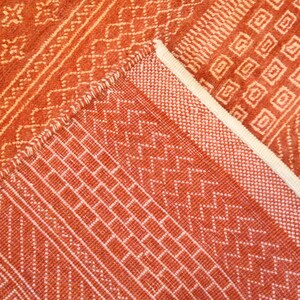 K&ouml;nnte beinhalten: Nahaufnahme eines roten und wei&szlig;en gewebten Teppichs mit geometrischem Muster. Der Teppich hat einen Fransenrand.
