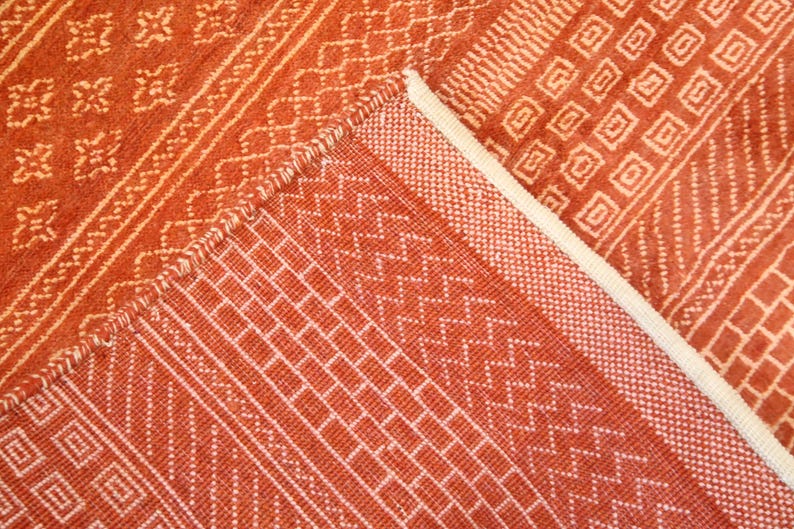 K&ouml;nnte beinhalten: Nahaufnahme eines roten und wei&szlig;en gewebten Teppichs mit geometrischem Muster. Der Teppich hat einen Fransenrand.
