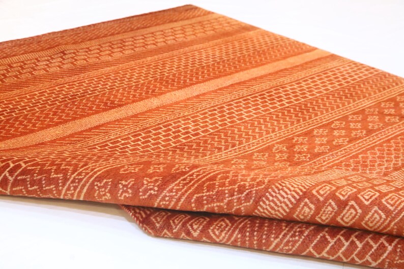 K&ouml;nnte beinhalten: Ein Nahaufnahme eines gefalteten orangefarbenen und wei&szlig;en Stoffes mit geometrischem Muster. Der Stoff ist weich und texturiert.