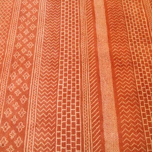 K&ouml;nnte beinhalten: Nahaufnahme eines roten Teppichs mit einem wei&szlig;en geometrischen Muster. Das Muster besteht aus sich wiederholenden Linien und Formen.