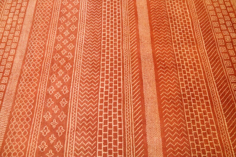 K&ouml;nnte beinhalten: Nahaufnahme eines roten Teppichs mit einem wei&szlig;en geometrischen Muster. Das Muster besteht aus sich wiederholenden Linien und Formen.