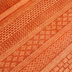 K&ouml;nnte beinhalten: Nahaufnahme eines roten und wei&szlig;en Teppichs mit verschiedenen geometrischen Mustern. Der Teppich hat einen dezenten Glanz und eine weiche Textur.