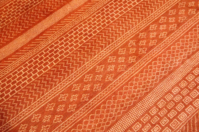 K&ouml;nnte beinhalten: Nahaufnahme eines roten und wei&szlig;en Teppichs mit verschiedenen geometrischen Mustern. Der Teppich hat einen dezenten Glanz und eine weiche Textur.