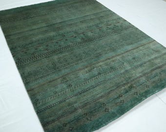 Op de afbeelding: Een rechthoekig, teal-kleurig tapijt met een verweerde uitstraling. Het tapijt heeft horizontale strepen en decoratieve patronen in donkerdere tinten teal en zwart. Het tapijt is gemaakt van een geweven materiaal.