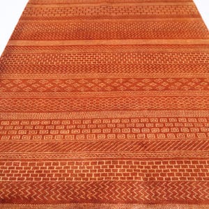 K&ouml;nnte beinhalten: Ein rot-orangener Teppich mit geometrischem Muster. Der Teppich hat verschiedene Muster, darunter Streifen, Quadrate und Rauten.