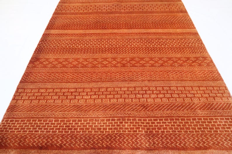 K&ouml;nnte beinhalten: Ein rot-orangener Teppich mit geometrischem Muster. Der Teppich hat verschiedene Muster, darunter Streifen, Quadrate und Rauten.