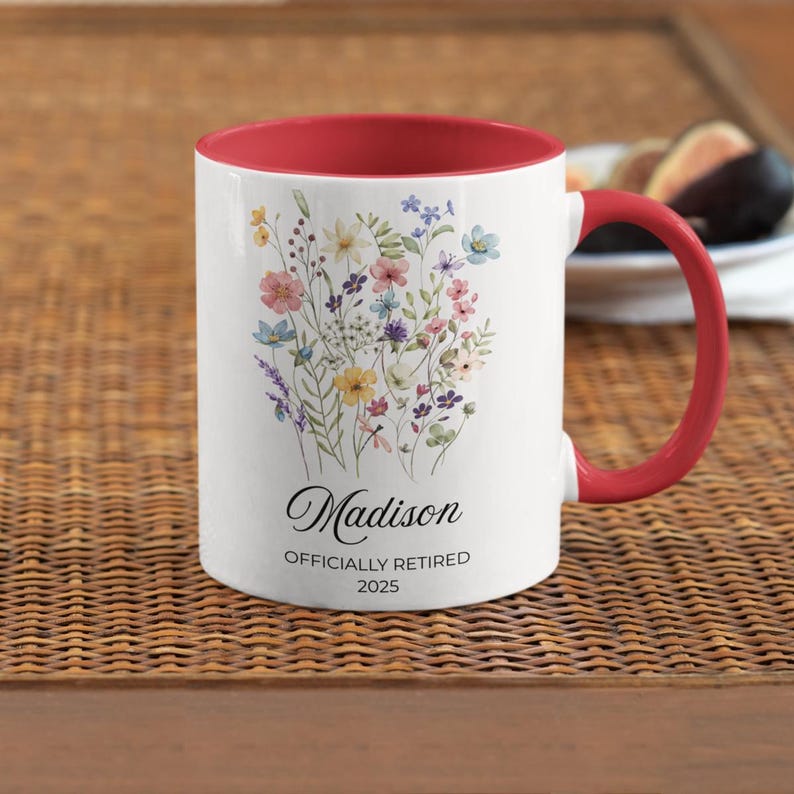 Op de afbeelding: Witte keramische mok met een rode binnenkant en handvat, versierd met een pastelkleurig bloemmotief. De mok is gepersonaliseerd met de naam "Madison" en de tekst "OFFICIALLY RETIRED 2025".