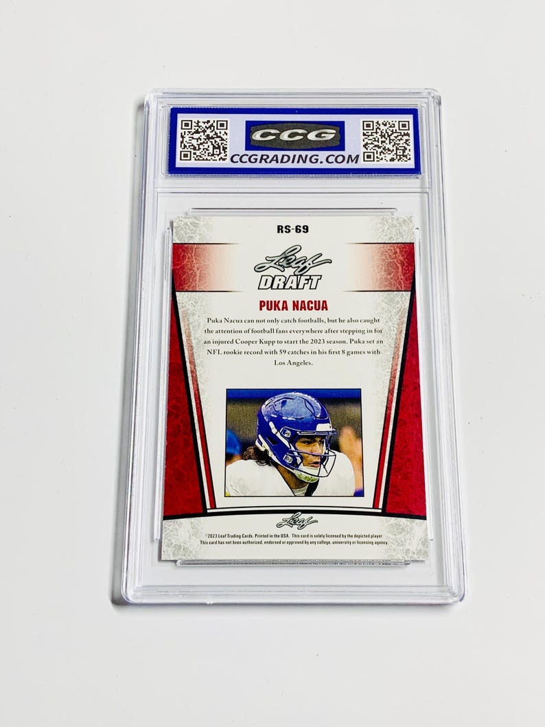 May include: A Puka Nacua football trading card, graded and encased in a protective holder. The card features a photo of the player in a blue helmet and the text "DRAFT PUKA NACUA". The card has red and white accents.