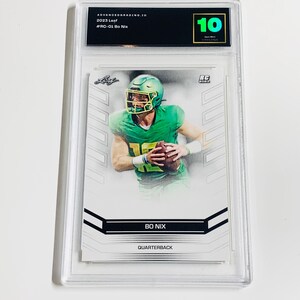 K&ouml;nnte beinhalten: Eine bewertete 2023 Leaf Bo Nix Footballkarte. Die Karte zeigt einen Spieler in gr&uuml;ner Uniform, der einen Football h&auml;lt. Die Karte ist in einem transparenten Kunststoffhalter eingeschlossen und mit 10 bewertet.