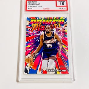 May include: A Kevin Durant Power Players trading card from 2025 Topps, graded Pristine 10. The card features Durant in a Phoenix Suns uniform, with a colorful background. The card is encased in a clear protective holder.