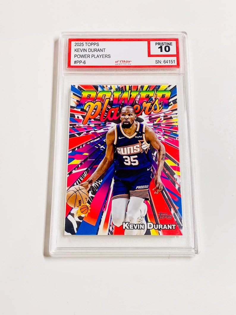 May include: A Kevin Durant Power Players trading card from 2025 Topps, graded Pristine 10. The card features Durant in a Phoenix Suns uniform, with a colorful background. The card is encased in a clear protective holder.