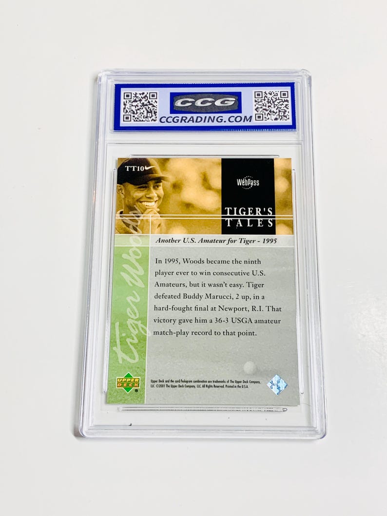 May include: A Tiger Woods trading card encased in a clear plastic holder. The card features a photo of Tiger Woods and text that reads "TIGER'S TALES" and "Another U.S. Amateur for Tiger - 1995". The card is graded by CCG.