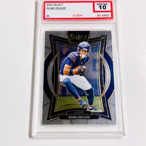 May include: A 2024 Select Rome Odunze football trading card, graded Pristine 10. The card features a player in a blue and white uniform. The card is encased in a clear protective holder.