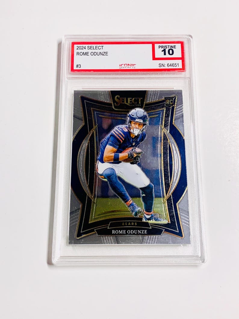 May include: A 2024 Select Rome Odunze football trading card, graded Pristine 10. The card features a player in a blue and white uniform. The card is encased in a clear protective holder.