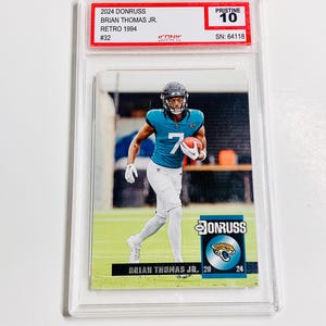 May include: A football trading card featuring Brian Thomas Jr. in a teal and white uniform, holding a football. The card is graded Pristine 10 and includes the text "2024 Donruss" and "Retro 1994".
