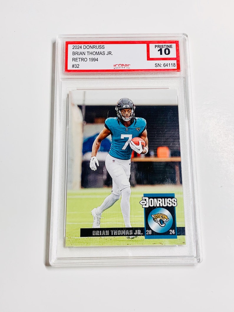 May include: A football trading card featuring Brian Thomas Jr. in a teal and white uniform, holding a football. The card is graded Pristine 10 and includes the text "2024 Donruss" and "Retro 1994".