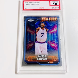 May include: A 2024 Topps Chrome Carmelo Anthony trading card, graded Pristine 10, encased in a protective holder. The card features a player in a New York jersey with the number 7. The card has a blue and silver design.