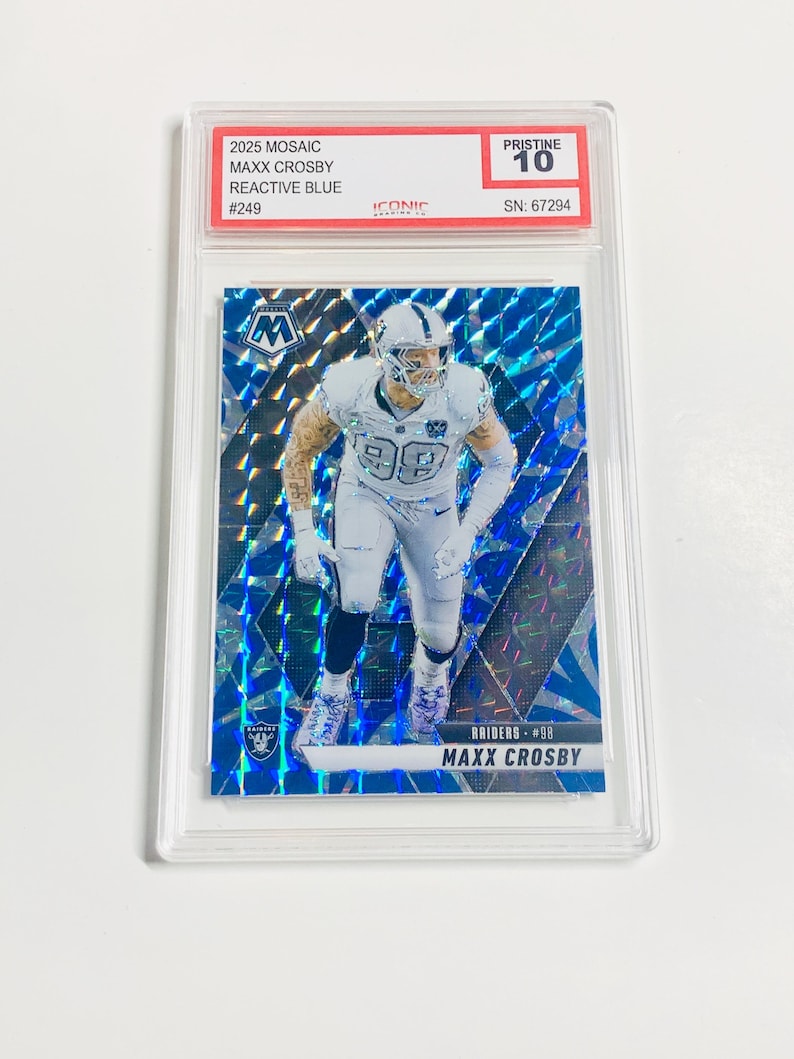 May include: A football trading card featuring Maxx Crosby in a white Raiders uniform. The card has a blue mosaic background and is graded Pristine 10. Text on the card includes "2025 Mosaic," "Reactive Blue," and "Raiders #98."