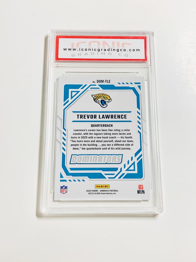 Op de afbeelding: Een beoordeelde trading card met Trevor Lawrence, een quarterback, met een blauw en wit ontwerp. De kaart zit in een doorzichtige plastic houder met het logo van "Iconic Grading Co.".