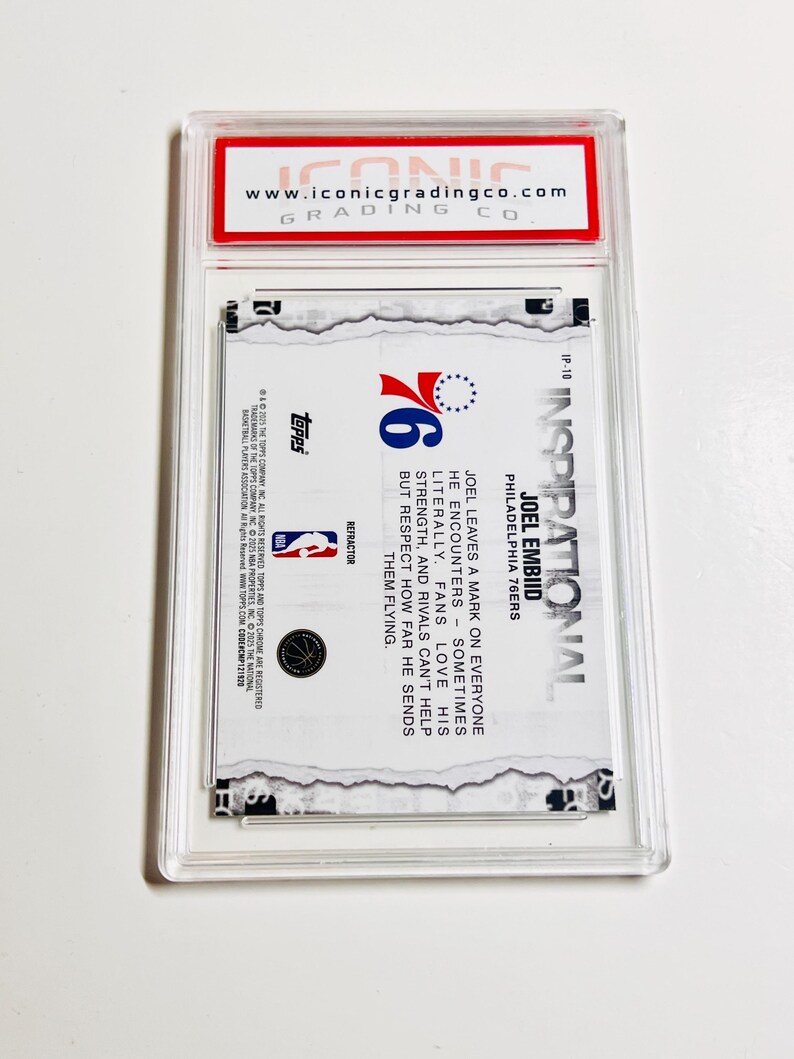 Puede incluir: Una tarjeta de baloncesto coleccionable dentro de un estuche de pl&aacute;stico transparente. La tarjeta presenta el logotipo de los 76ers de Filadelfia y texto sobre Joel Embiid. La parte superior del estuche tiene una etiqueta roja con el sitio web "www.iconicgradingco.com".